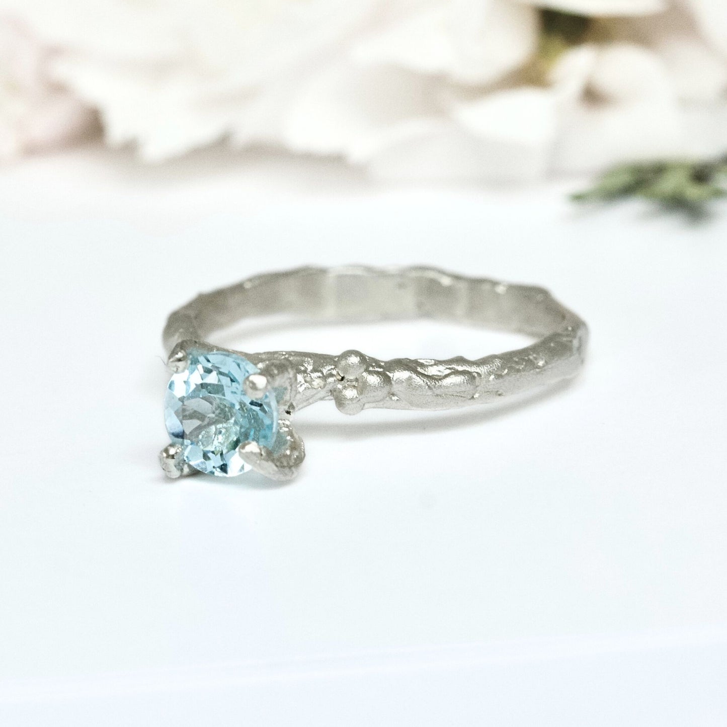 Textured four claw silver ring with blue topaz gemstone.