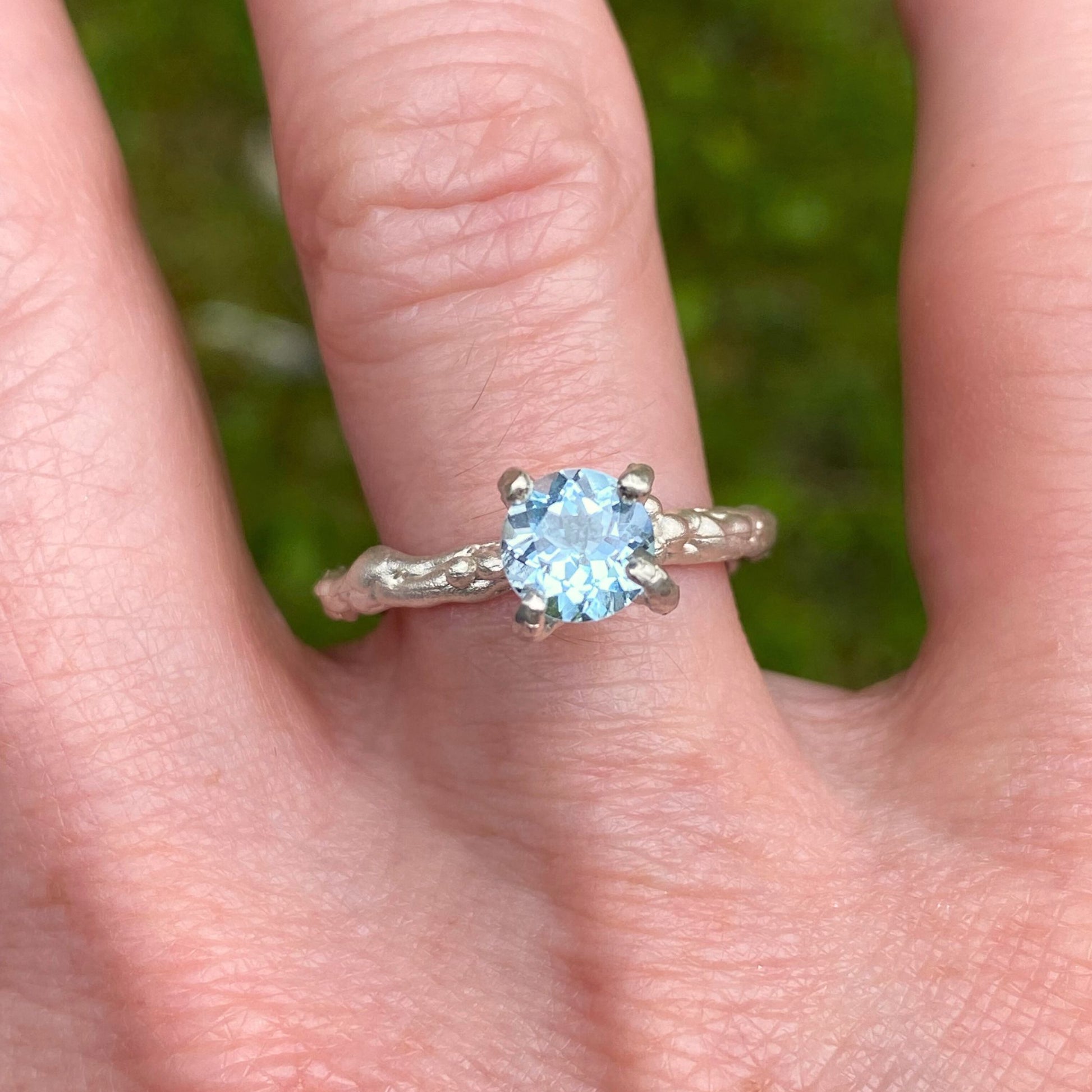 Textured four claw silver ring with blue topaz gemstone.